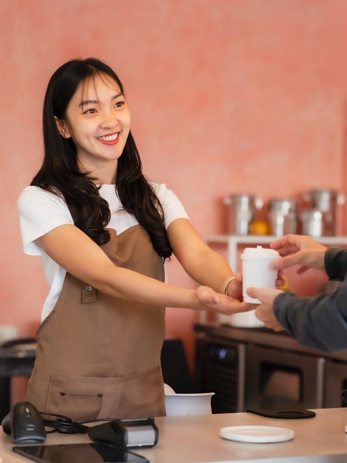 Business Owner Concept - Barista offers disposable take away hot coffee at the modern coffee shop.